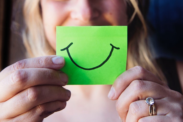 Žena drží pred tvárou zelený papierik s úsmevom.jpg